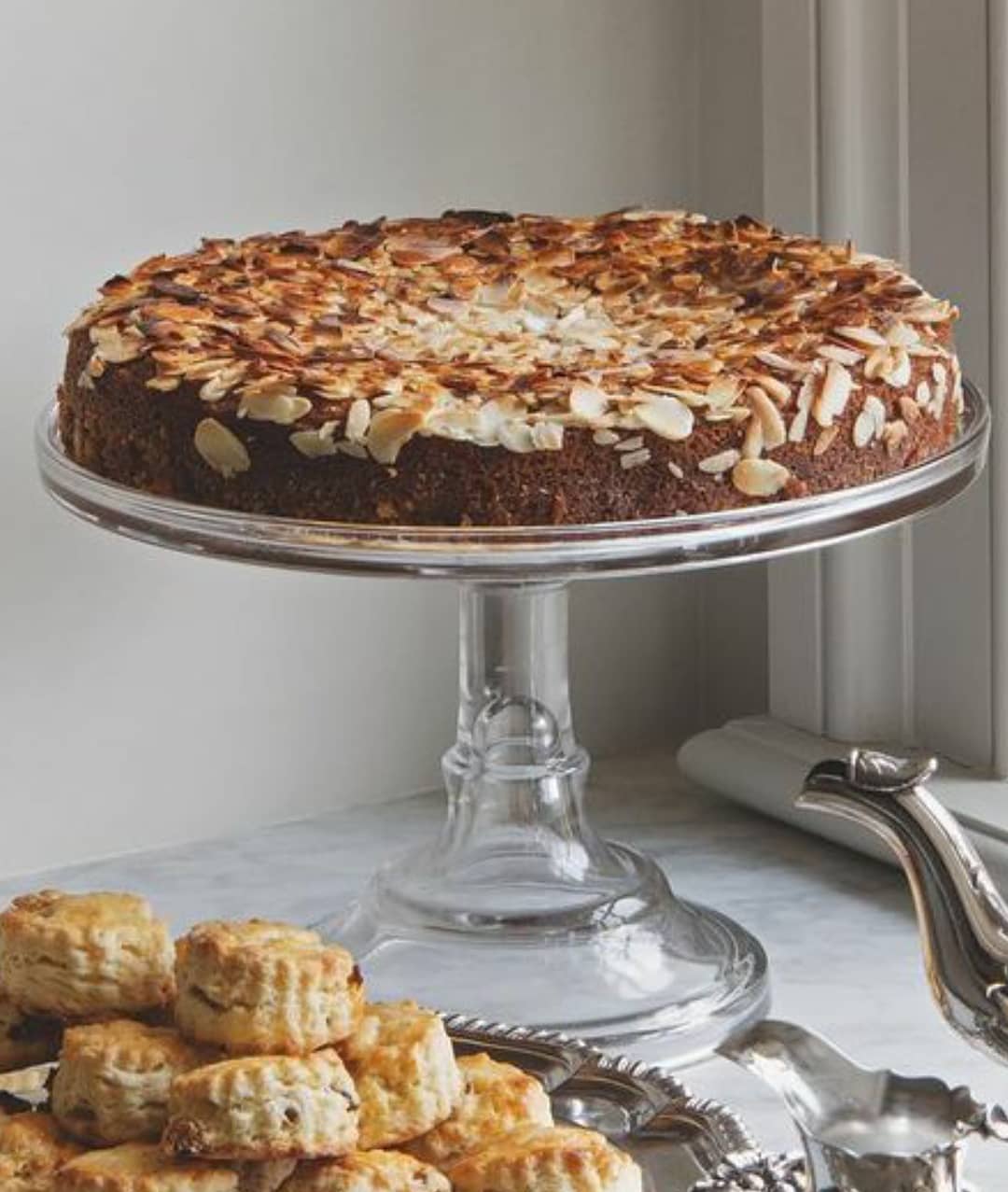 Tarta decorada sobre pedestal de cristal con dulces variados. Especialistas en listas de boda Cuidada selección de artículos de mesa y decoración